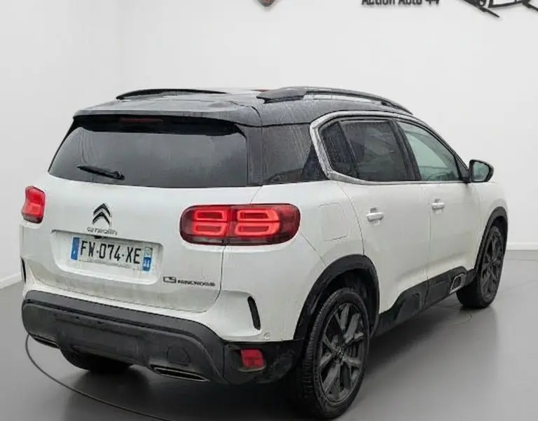 Vue 3/4 arrière droite d’un Citroën C5 Aircross blanc nacré avec toit noir et feux arrière LED allumés dans un studio.
