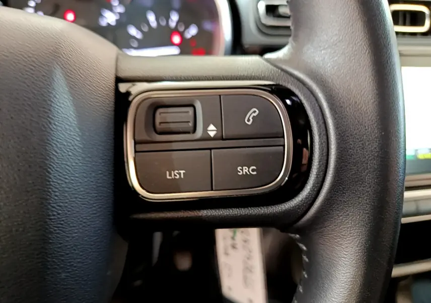 Gros plan sur les commandes gauche du volant cuir de la Citroën C3 blanche, avec boutons de téléphone et liste.