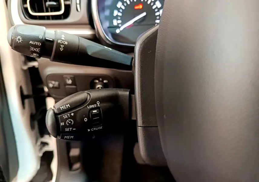 Gros plan sur les commandes de régulateur de vitesse et phares à gauche du volant d'une Citroën C3 blanche de 2019.