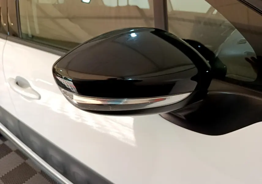Rétroviseur noir brillant côté conducteur sur une Citroën C3 blanche vue de profil rapproché.
