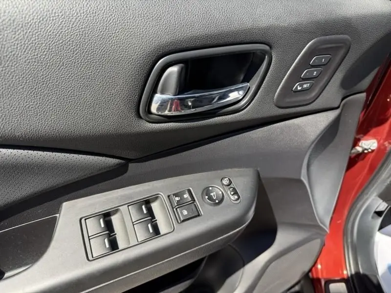 Vue rapprochée de la porte avant gauche du Honda CR-V rouge métal 2017, montrant les commandes de vitres et réglages mémoire.