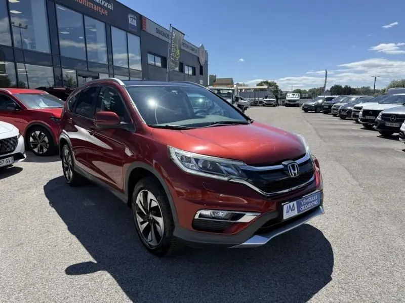 Honda CR-V rouge métal vue 3/4 avant droit, avec calandre noire et jantes alliage distinctives, sur parking extérieur.