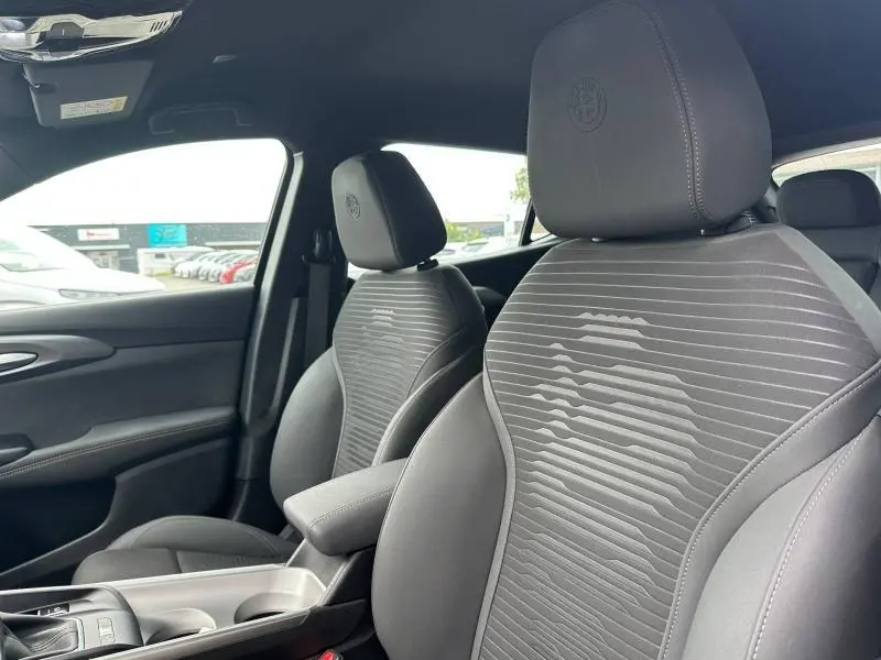 Vue intérieure côté droit des sièges avant gris foncé de l'Alfa Romeo Tonale 1.5 Hybrid 2025 avec logo brodé sur les appuie-têtes.