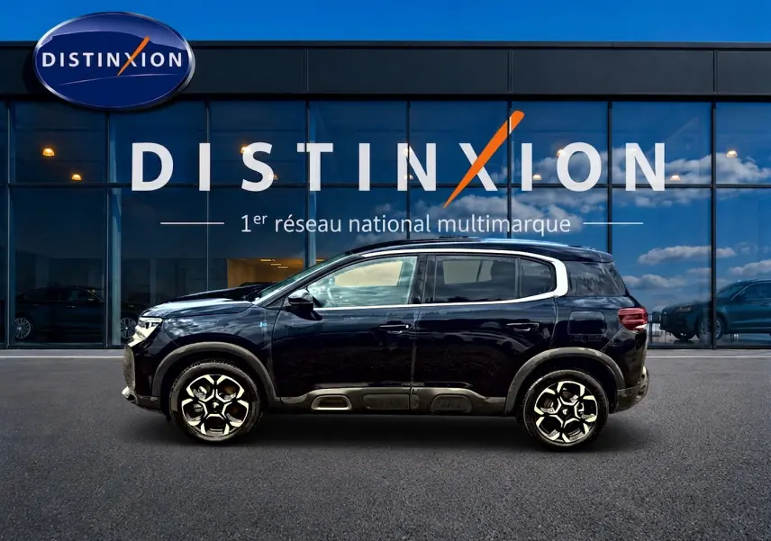 Profil latéral droit du Citroën C5 Aircross noir 2024 avec jantes alu et barres de toit visibles devant une vitrine Distinxion.