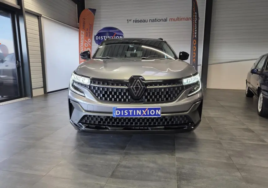 Vue de face du Renault Austral gris foncé avec calandre damier ice black et feux LED allumés en showroom.