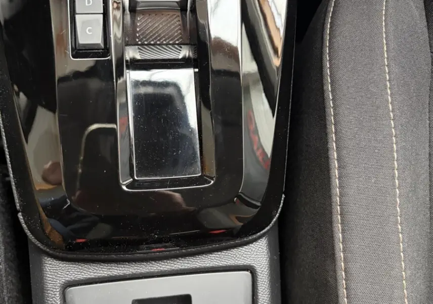 Gros plan sur la console centrale noire brillante avec levier de boîte auto et frein à main électrique, siège tissu gris visible.