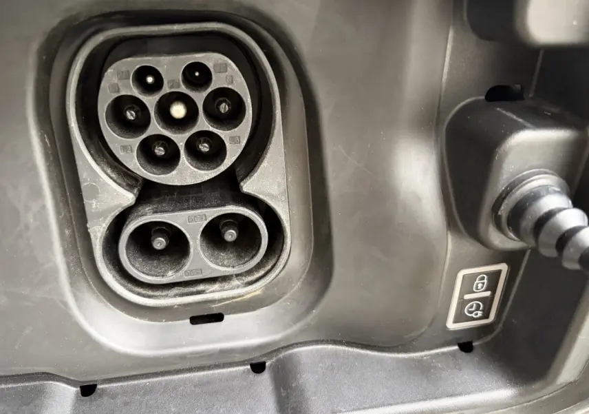 Gros plan sur la prise de charge électrique noire du Citroën C3 Aircross gris foncé, avec câble branché visible.