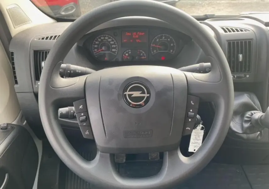 Vue rapprochée du volant noir d'un Opel Movano Fourgon blanc, avec commandes intégrées et tableau de bord visible.