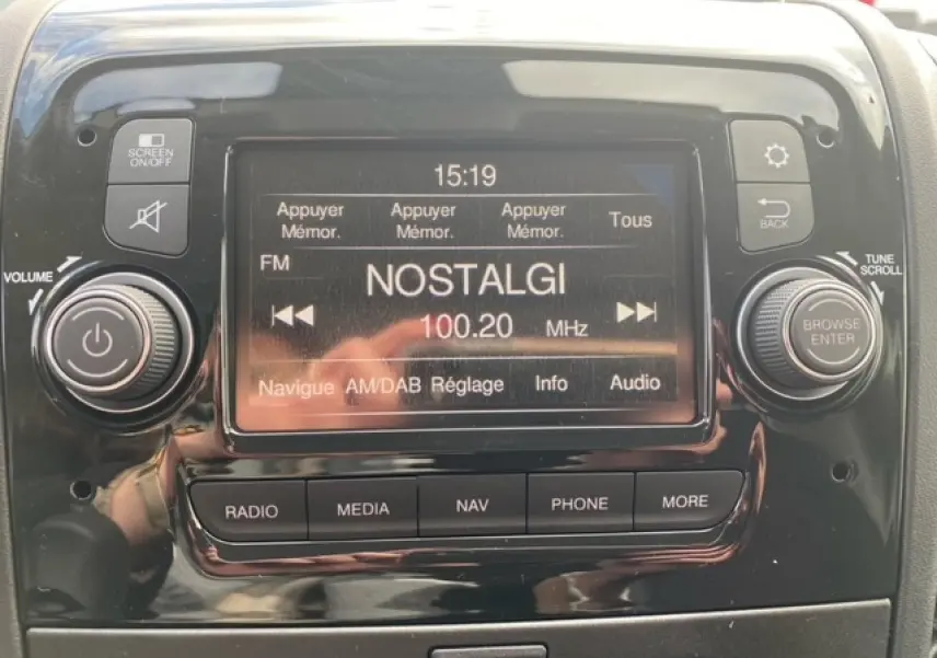 Détail de l'écran tactile central du système multimédia du fourgon Opel Movano blanc, affichant la radio FM sur la fréquence 100.20 MHz.