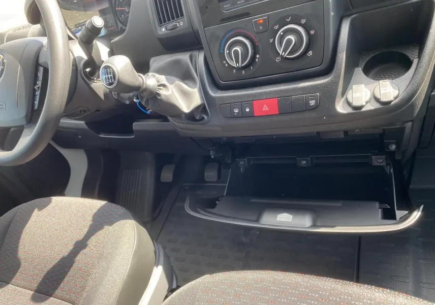 Intérieur Opel Movano Fourgon 2023 vu côté passager, tableau de bord noir avec boîte à gants ouverte et levier de vitesses manuel.