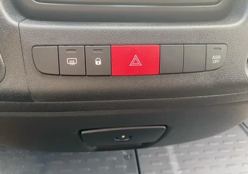 Gros plan sur les boutons de commande du tableau de bord noir de l'Opel Movano Fourgon blanc, avec bouton rouge de warning central.