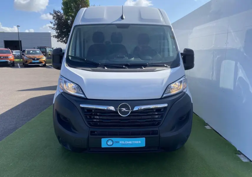 Vue frontale d'un Opel Movano Fourgon blanc 2023 avec calandre noire et logo Opel visible sur parking.
