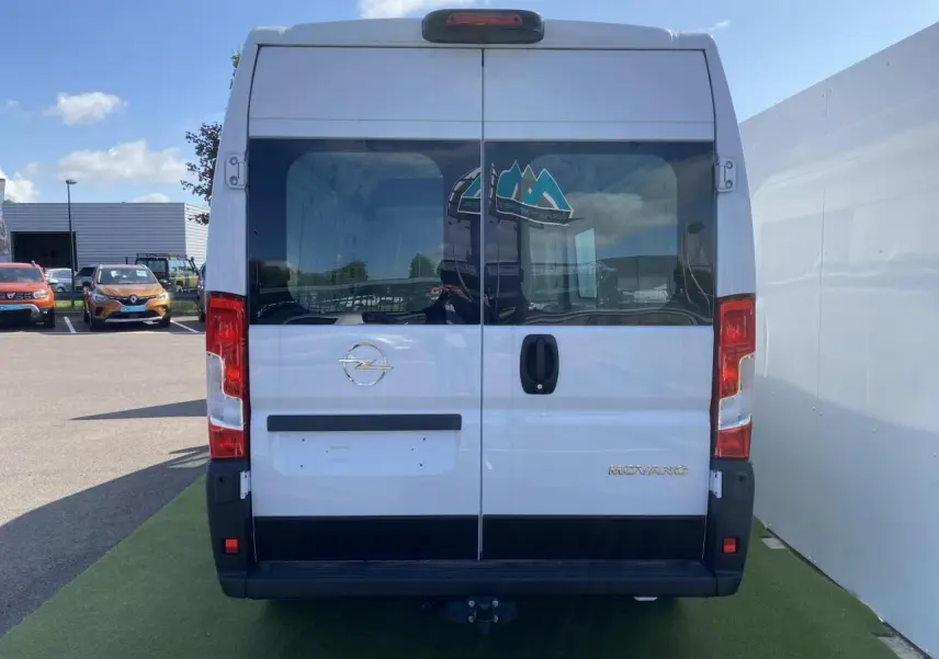Vue arrière d'un Opel Movano Fourgon blanc avec portes vitrées battantes et crochet d'attelage visible.