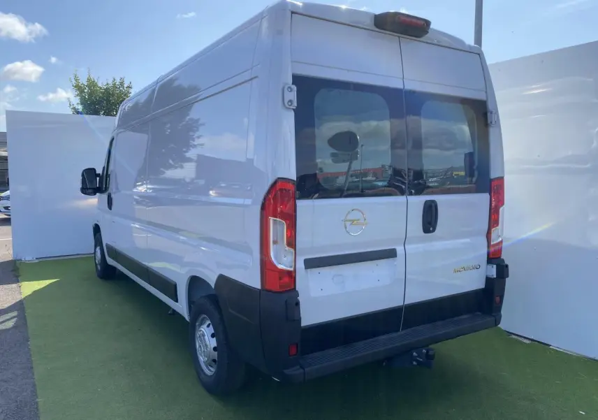 Vue 3/4 arrière droite d'un Opel Movano Fourgon blanc avec portes vitrées et crochet d'attelage visible.