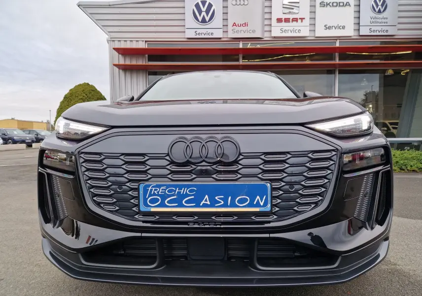 Vue frontale d'un Audi Q6 e-tron Performance S-Line gris Manhattan avec calandre noire et phares LED allumés.