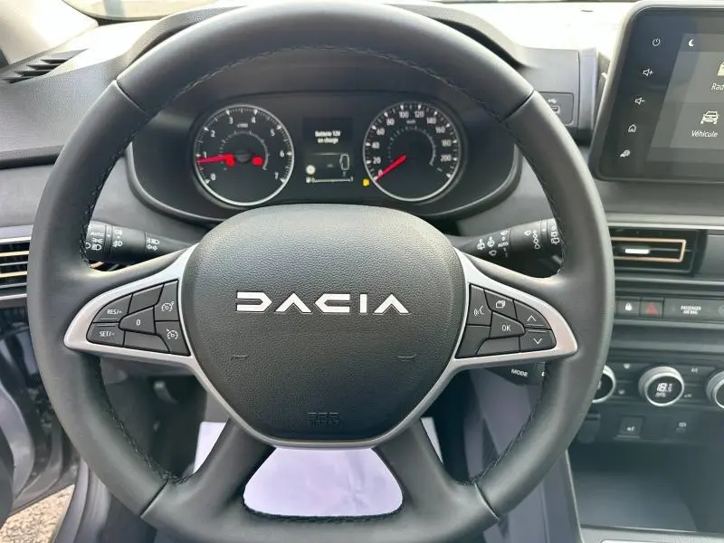 Vue rapprochée du volant DACIA avec commandes intégrées, tableau de bord et écran tactile du Sandero 2025 en intérieur.