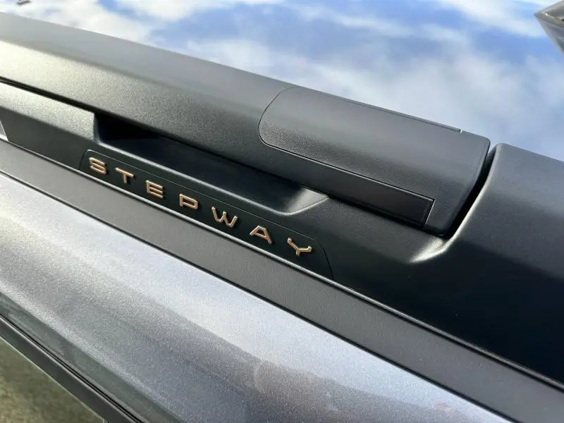 Gros plan sur l'inscription Stepway en relief bronze sur la barre de toit noire du Dacia Sandero gris schiste métallisé.