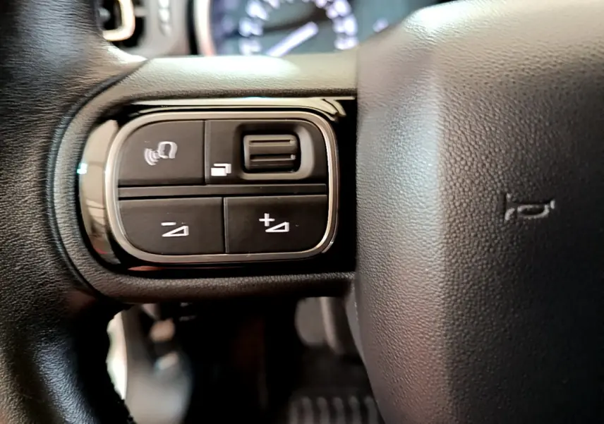 Gros plan sur les commandes gauche du volant cuir de la Citroën C3 blanche, modèle 2019, avec boutons multifonctions.
