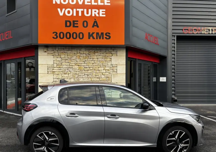Profil côté gauche d'une Peugeot 208 Hybrid 110 e-DCS6 GT gris clair, avec jantes noires et détails GT visibles.