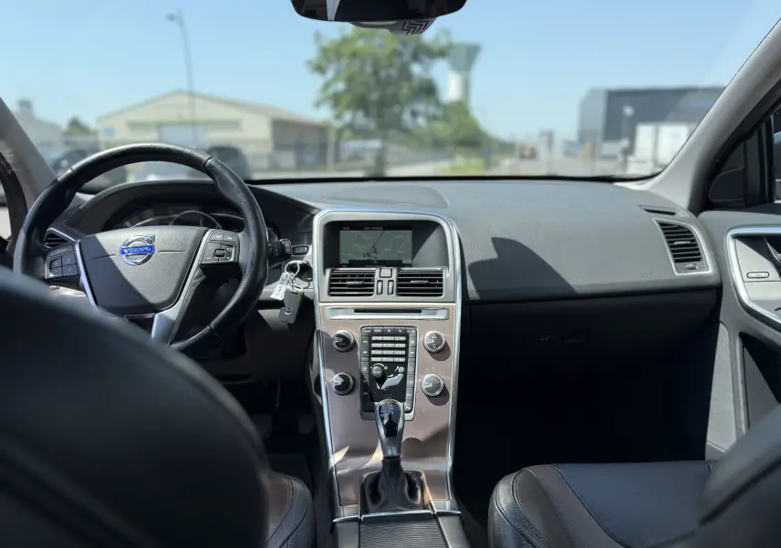 Vue intérieure avant du Volvo XC60 gris foncé 2016, mettant en valeur le tableau de bord et la console centrale avec écran intégré.