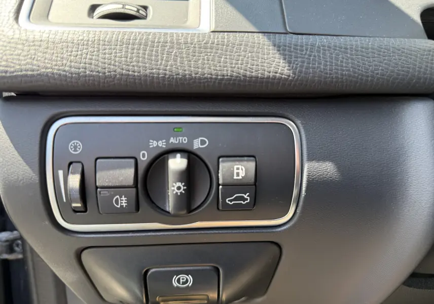 Détail du tableau de bord du Volvo XC60 2016 gris foncé, montrant les commandes d’éclairage et de parking électrique.