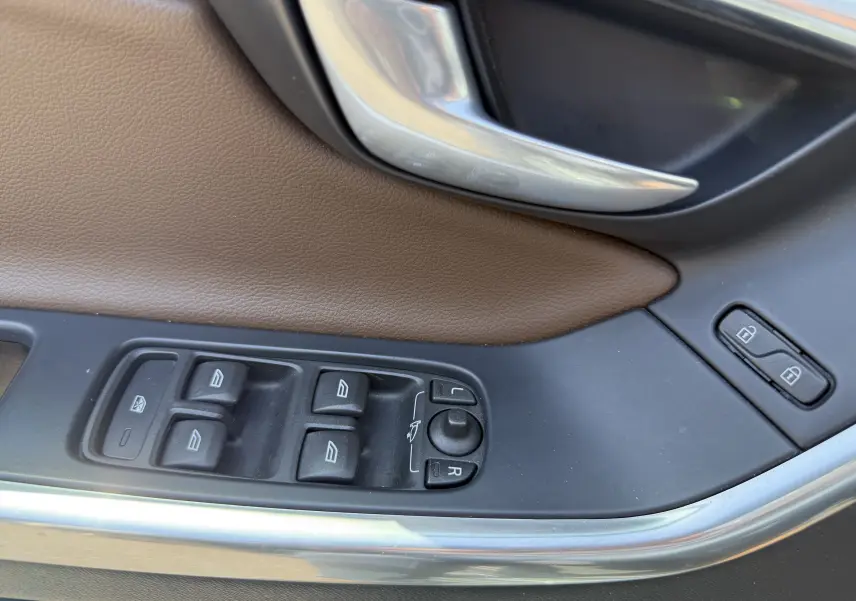 Gros plan sur la commande des vitres et rétroviseurs côté gauche, garniture cuir marron et poignée argentée du Volvo XC60 gris foncé.