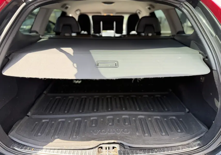 Vue arrière du coffre ouvert d'un Volvo XC60 gris foncé, avec cache-bagages et tapis de sol marqué VOLVO.