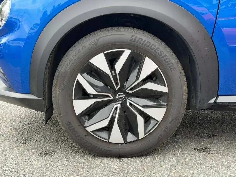 Gros plan sur la roue avant gauche du Nissan Juke 2025 bleu Magnétique avec jante noire et argentée au design géométrique.