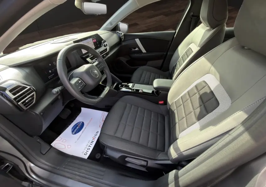 Vue intérieure côté conducteur de la Citroën C4 hybride 2025, sièges gris bi-ton et tableau de bord moderne avec écran tactile.