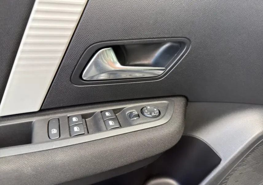 Gros plan sur la poignée intérieure et les commandes de vitres côté conducteur d'une Citroën C4 hybride 2025, finition gris foncé.