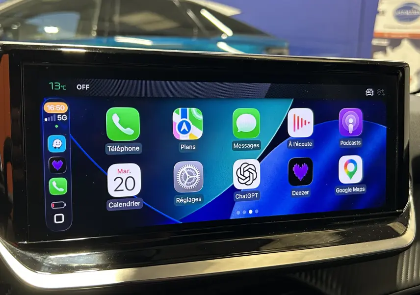 Écran tactile intérieur du Peugeot 208 II Turbo 100 Allure, affichant les applications connectées avec reflet d'une voiture grise en arrière-plan.