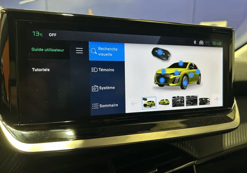 Écran tactile intérieur montrant l'interface d'aide visuelle avec une Peugeot 208 jaune en vue 3/4 avant.