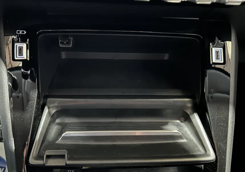 Vue rapprochée de la console centrale noire du Peugeot 208 II Turbo 100 Allure, avec ports USB visibles de chaque côté.
