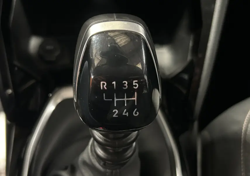 Gros plan sur le levier de vitesses manuel noir de la Peugeot 208 II Turbo 100 Allure, montrant les six rapports et la marche arrière.