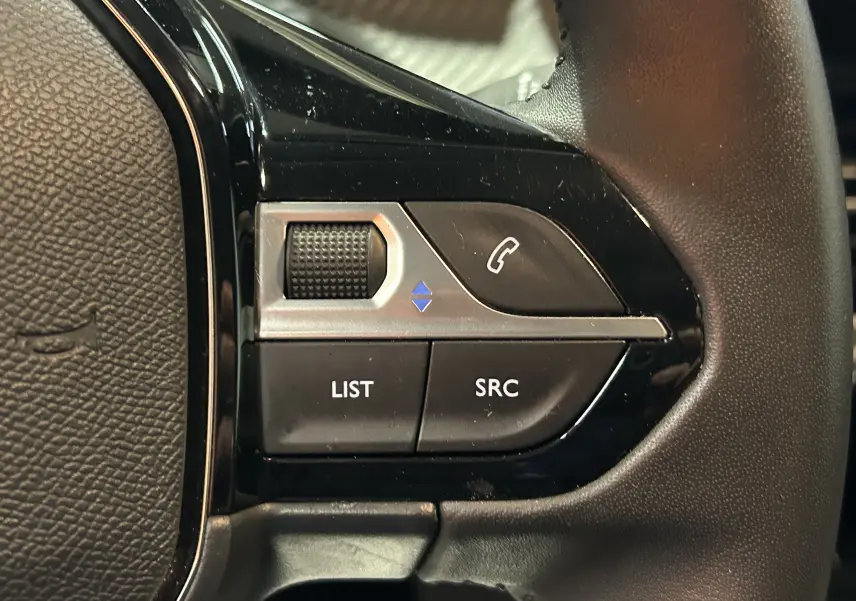 Gros plan sur les commandes au volant noir de la Peugeot 208 II Turbo 100 Allure, boutons LIST, SRC et téléphone.