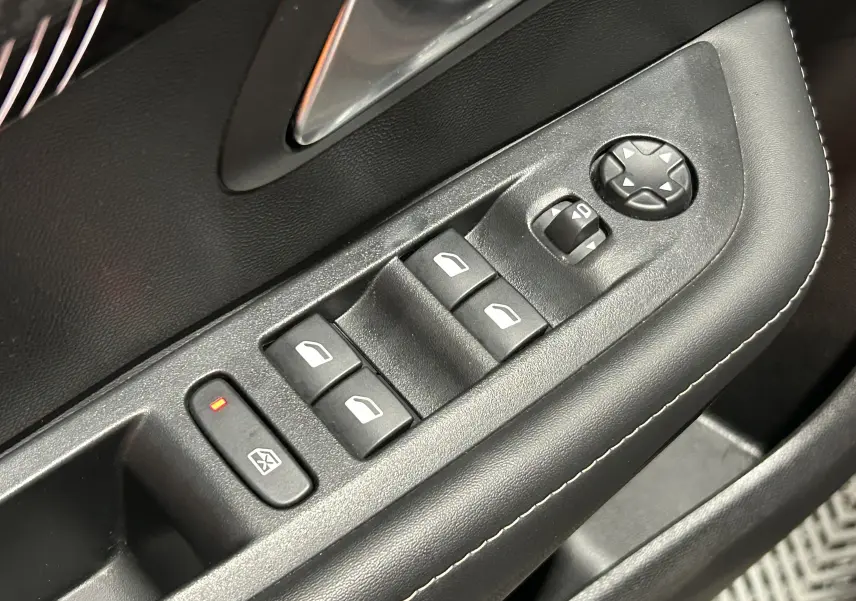 Gros plan sur la commande des vitres électriques et réglages des rétroviseurs côté conducteur, garniture noire avec surpiqûres blanches.