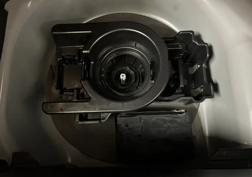 Gros plan sur le rangement sous le coffre d’un Peugeot 208 gris Selenium, montrant l’emplacement de la roue de secours et des outils.