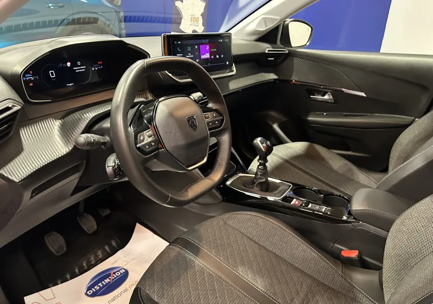 Intérieur de la Peugeot 208 II Turbo 100 Allure 2025, vue côté conducteur, volant cuir, écran tactile et boîte manuelle.