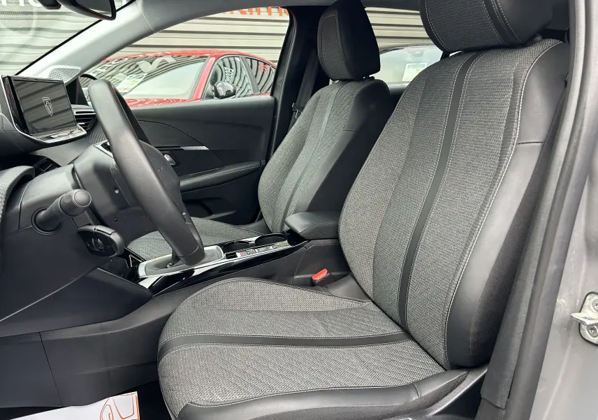 Vue intérieure côté conducteur de la Peugeot 208 gris Selenium, mettant en valeur les sièges tissu et cuir ainsi que la console centrale moderne.