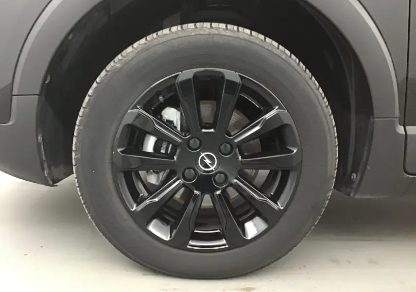 Gros plan sur la roue avant gauche noire d'un Opel Crossland 2022 avec jante alliage noire brillante et logo Opel central.