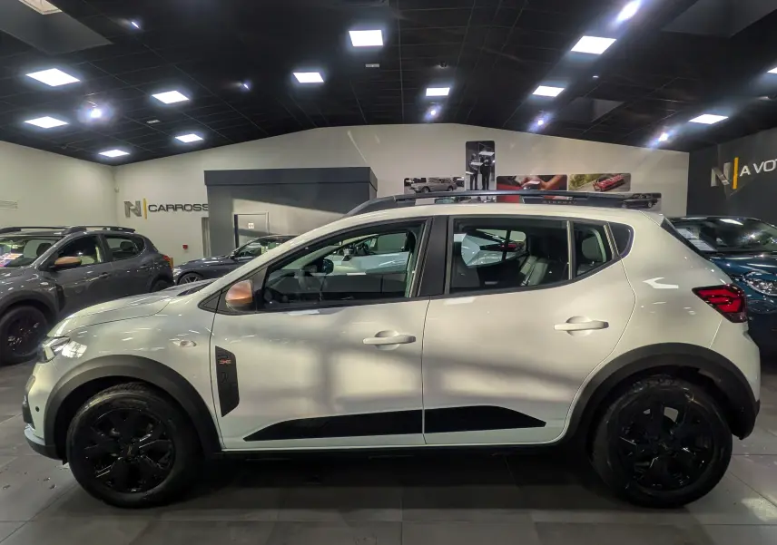 Profil latéral droit d'une Dacia Sandero Stepway TCe 110 blanche Glacier avec jantes noires et détails noirs contrastants en concession.