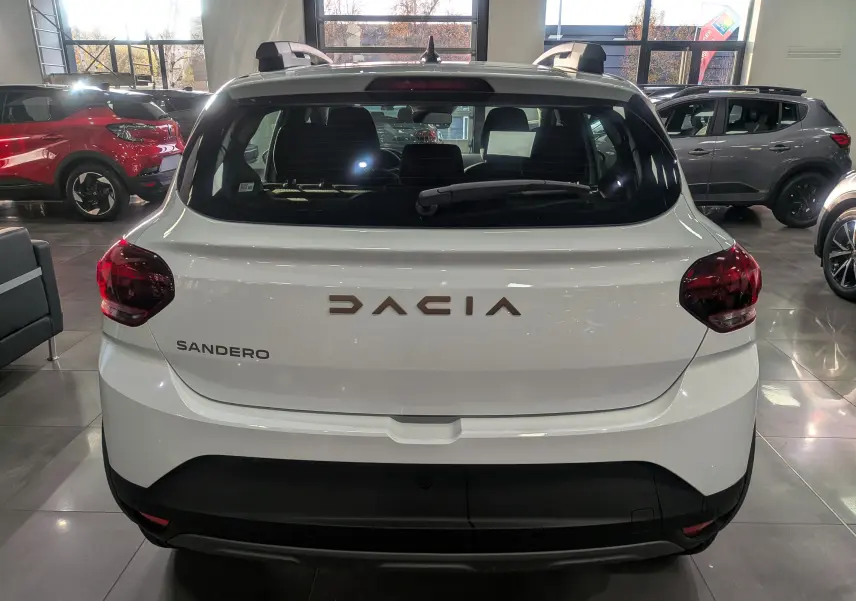 Vue arrière d'une Dacia Sandero Stepway blanc glacier en showroom, avec feux arrière rouges et lunette arrière dégagée.