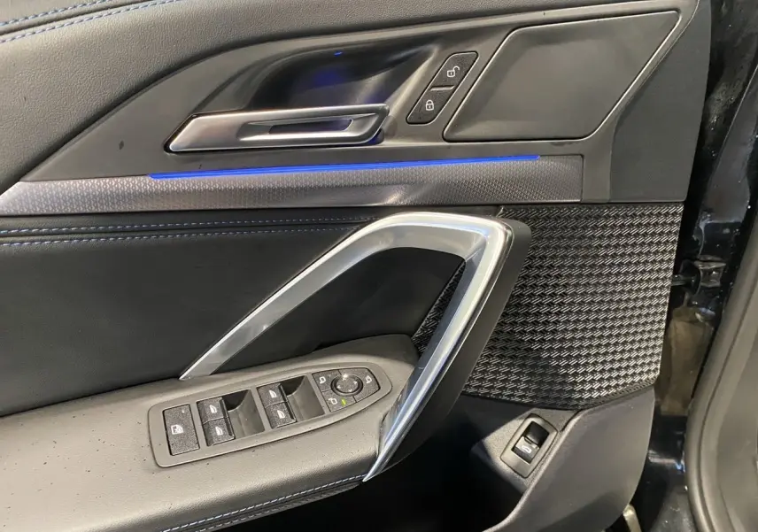 Détail de la porte côté gauche du BMW X1 2025 noir Saphire, avec commandes de vitres et éclairage d'ambiance bleu.