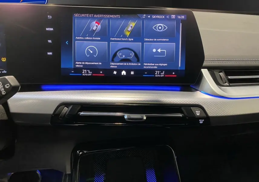 Tableau de bord intérieur de BMW X1 2025 avec écran tactile affichant les alertes de sécurité, ambiance lumineuse bleue.