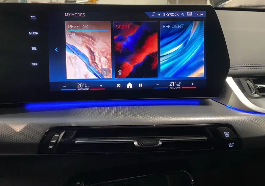 Écran tactile central du tableau de bord du BMW X1 2025 avec ambiance lumineuse bleue et commandes climatisation visibles.