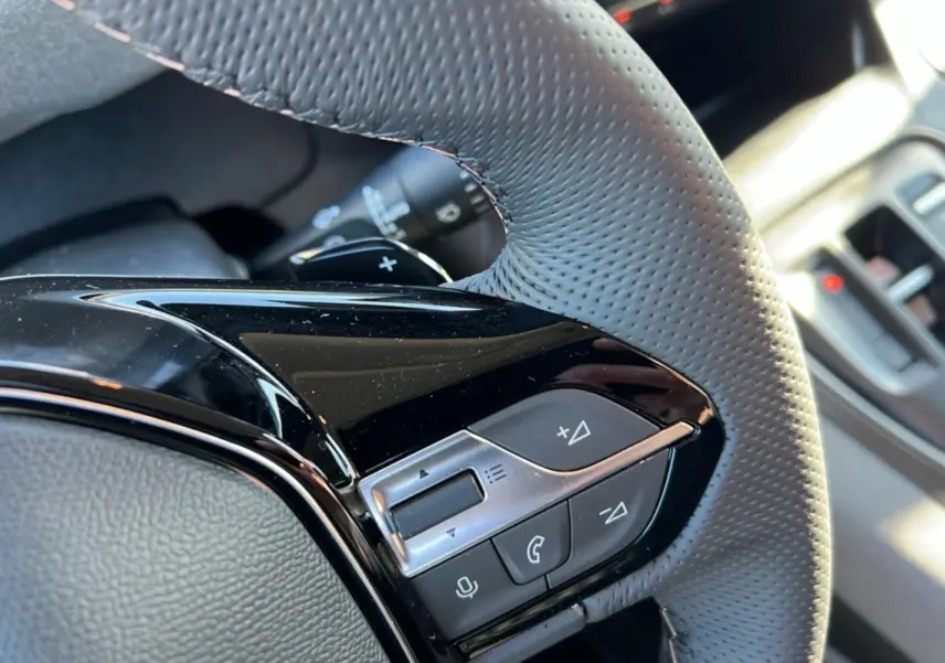 Gros plan sur les commandes multifonctions en plastique noir et gris du volant cuir perforé du Peugeot Rifter 2025.