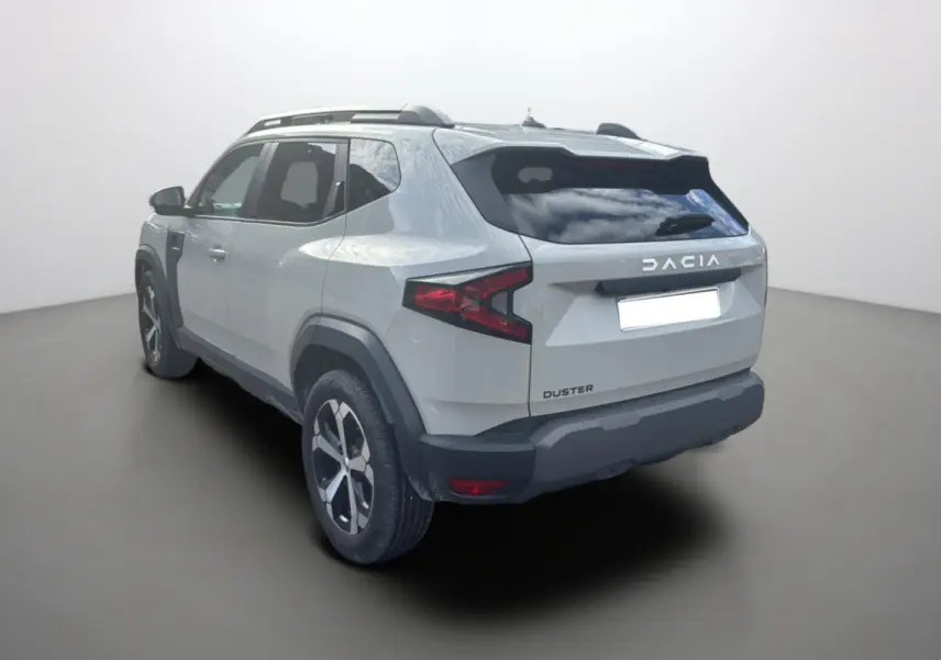 Vue 3/4 arrière droite d’un Dacia Duster 2025 couleur Sandstone avec barres de toit et jantes alu 18 pouces.