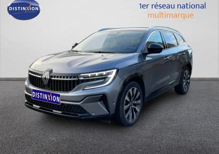 Renault Espace gris 2024 en 3/4 avant droit, avec jantes aluminium et barres de toit visibles.