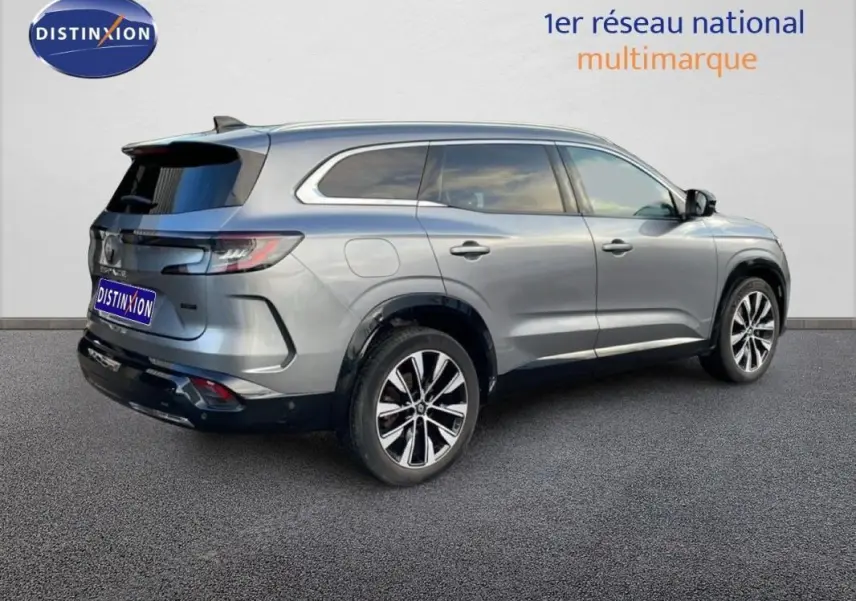 Vue 3/4 arrière droite d'un Renault Espace gris 2024 avec jantes aluminium et barres de toit visibles.