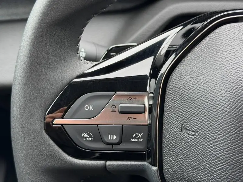 Gros plan sur les commandes multifonctions à gauche du volant noir de la Peugeot 308 Hybrid 2025, finition brillante.